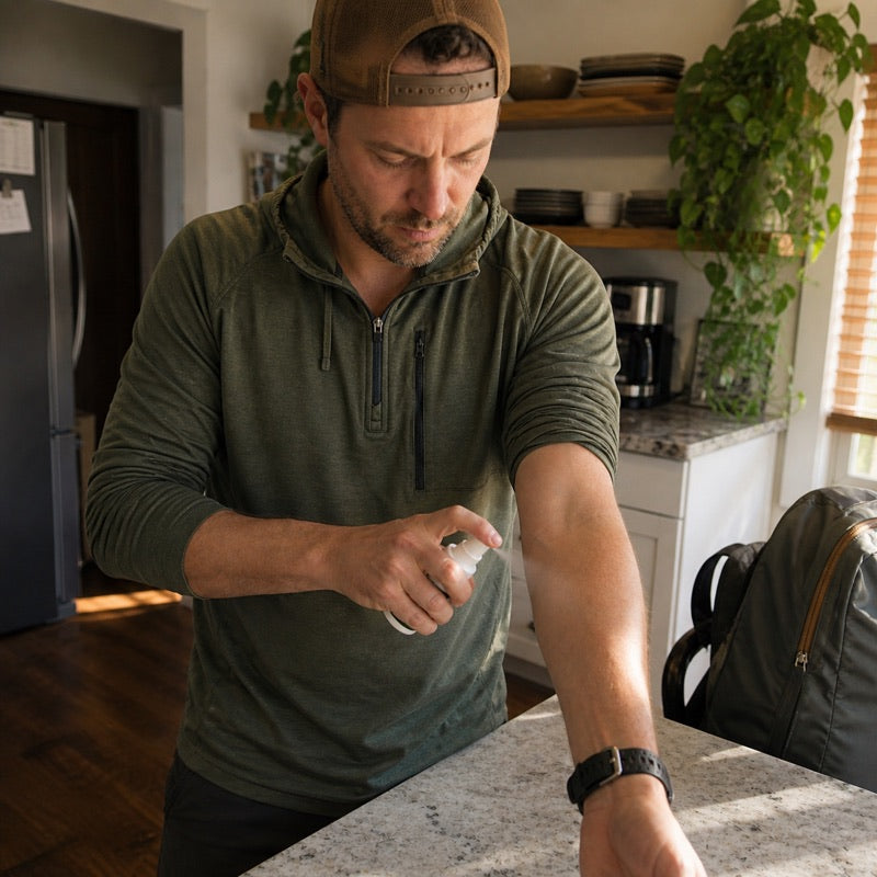Spraying his own forearm at the kitchen counter